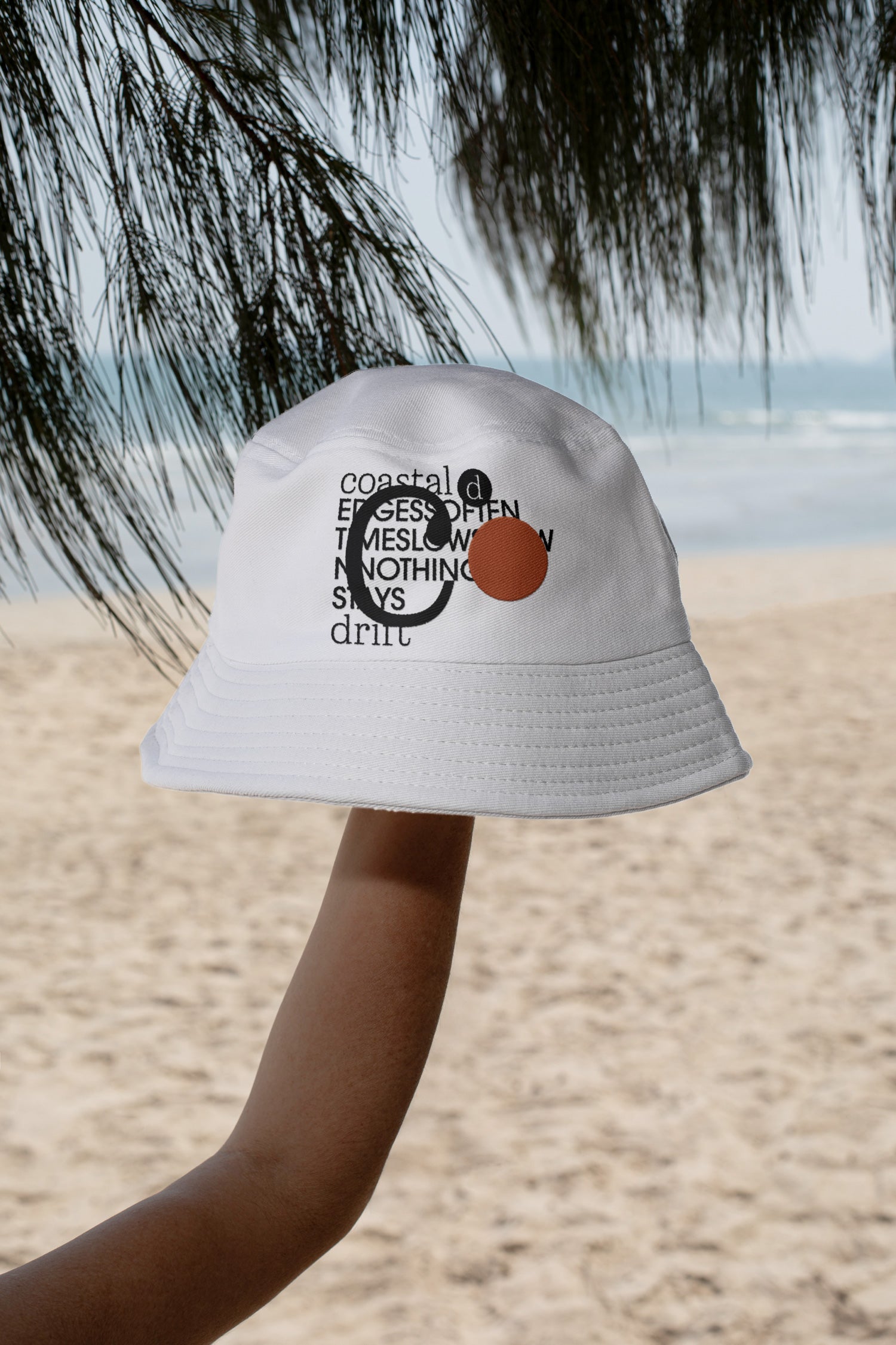 Bucket hat mockup held by hand against the coastline of Hua Hin, Thailand. Includes a realistic embroidery effect for presenting logos, apparel branding, and merchandise designs.