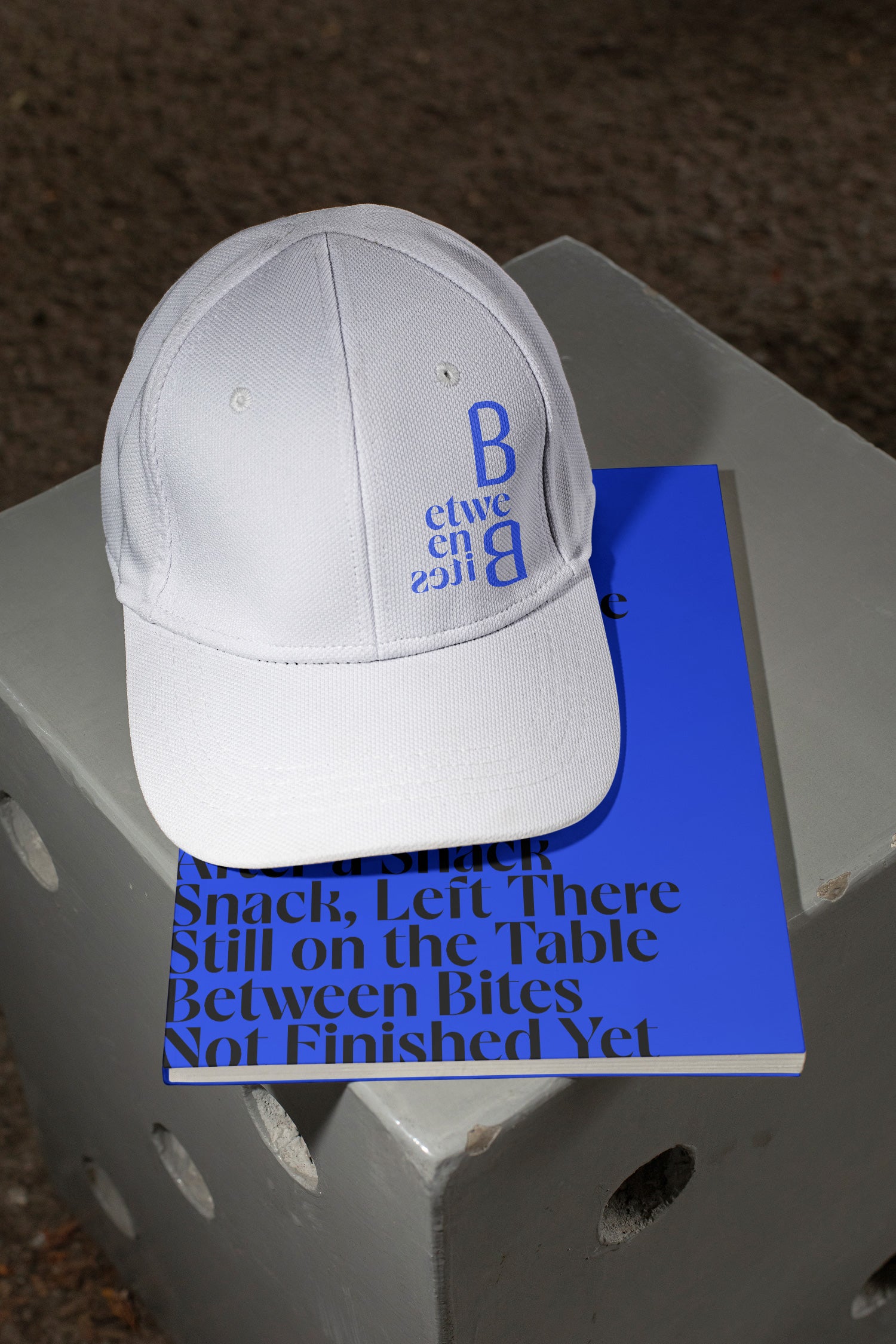 Two mockups in one featuring a cap and softcover magazine on a concrete chair.