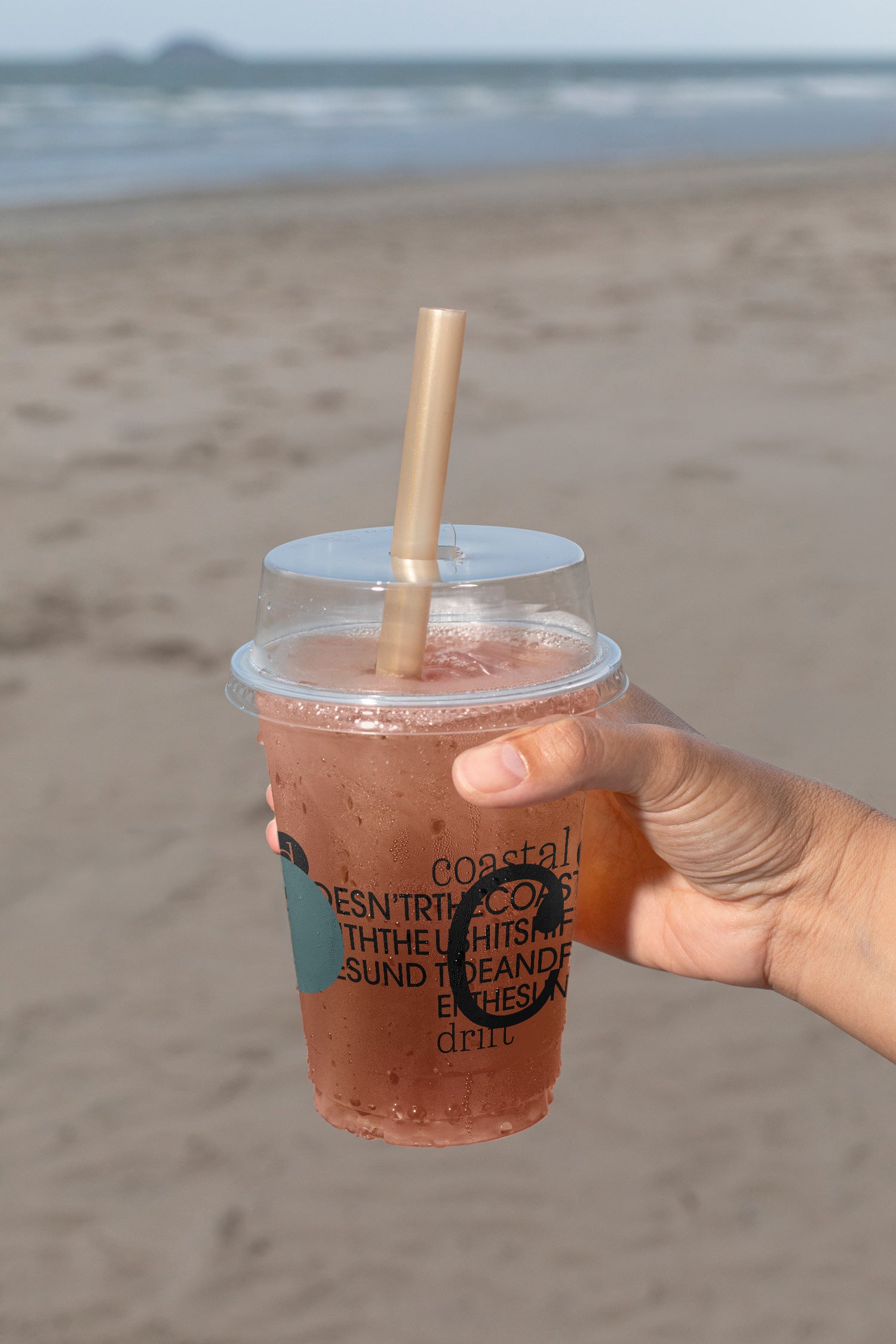 Plastic cup mockup held by hand at the beach. Built for showcasing beverage branding, logos, packaging, and summer lifestyle concepts.