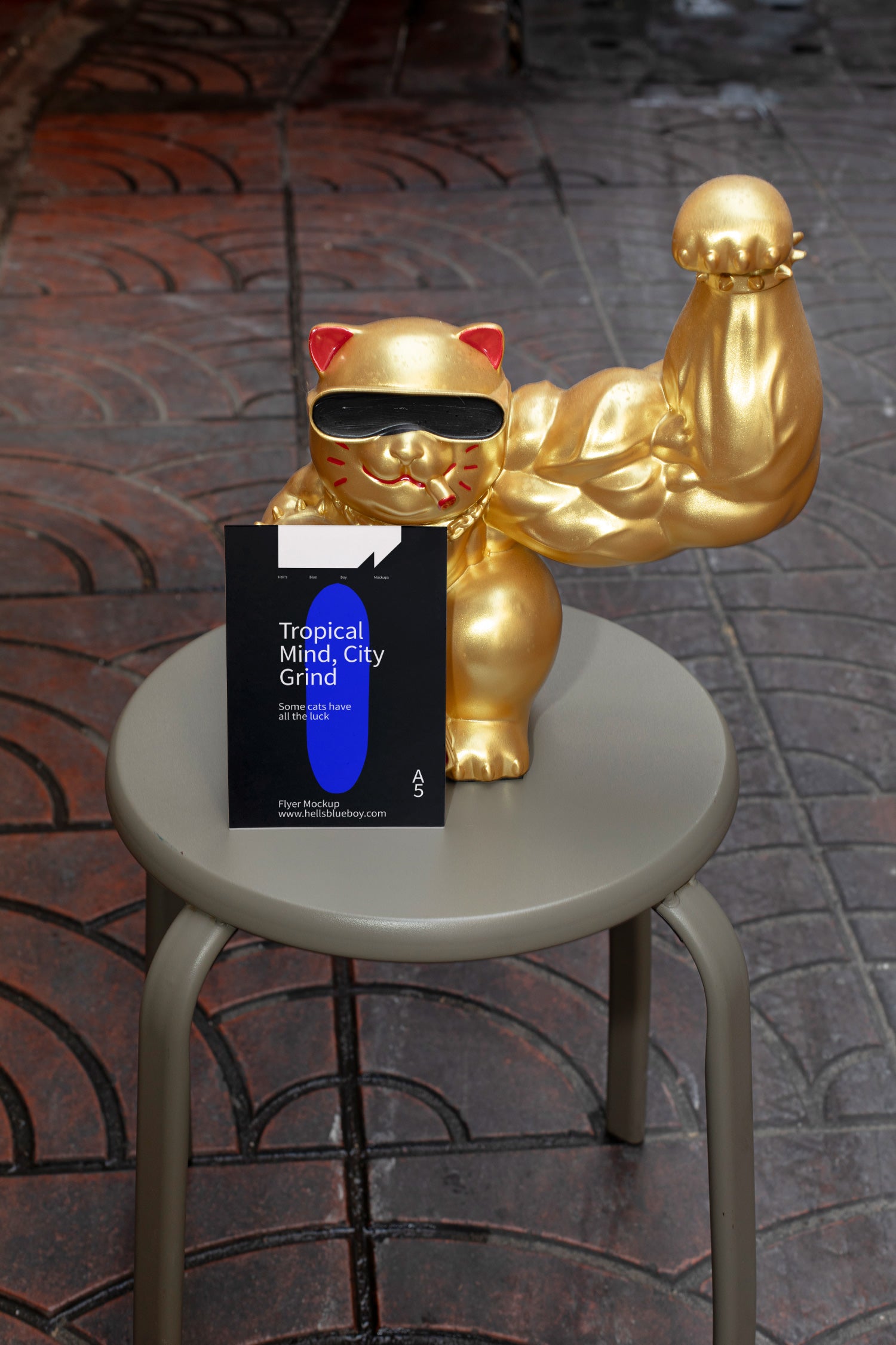 Street-style scene with a giant golden lucky cat sporting a muscular arm and holding a flyer, set on a chair against a tiled pavement background.