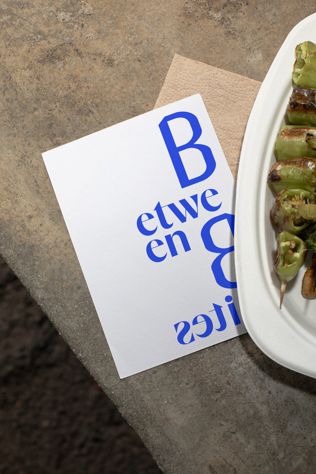 Flyer mockup lying on a concrete table beside grilled vegetables.