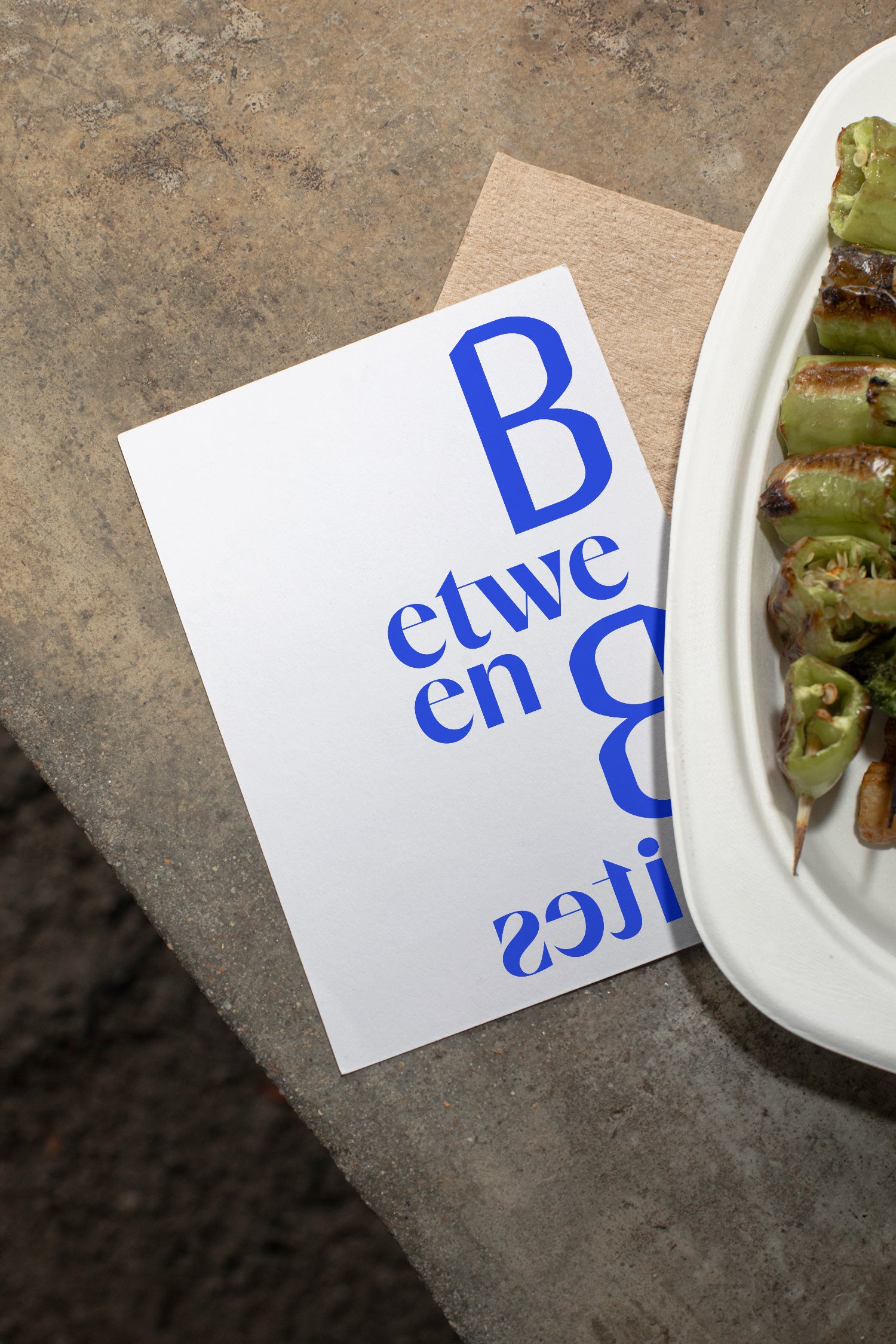 Flyer mockup lying on a concrete table beside grilled vegetables.