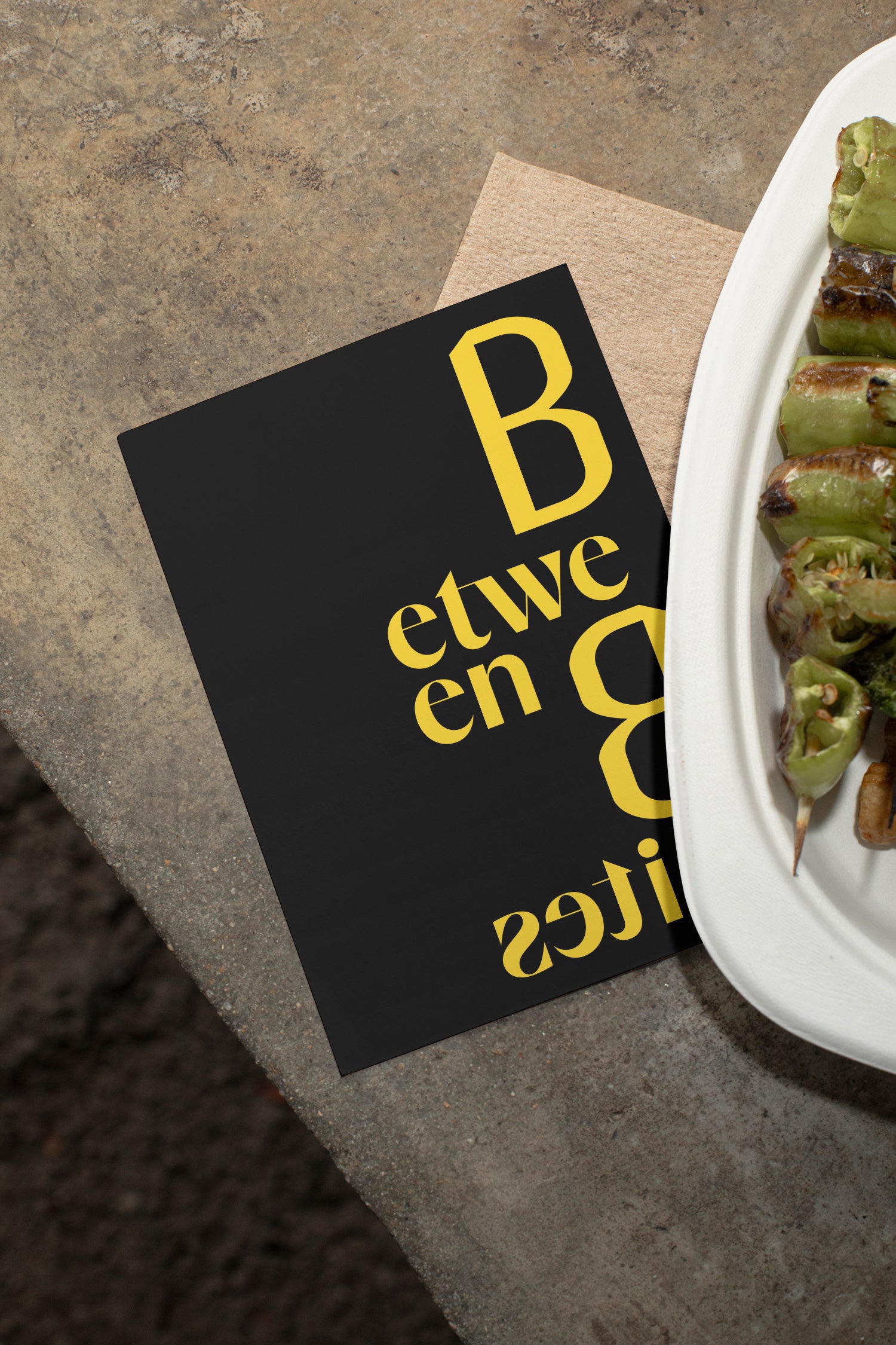Flyer mockup lying on a concrete table beside grilled vegetables.