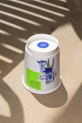Paper coffee cup mockup featuring stickers placed directly on the cup, photographed under harsh sunlight.