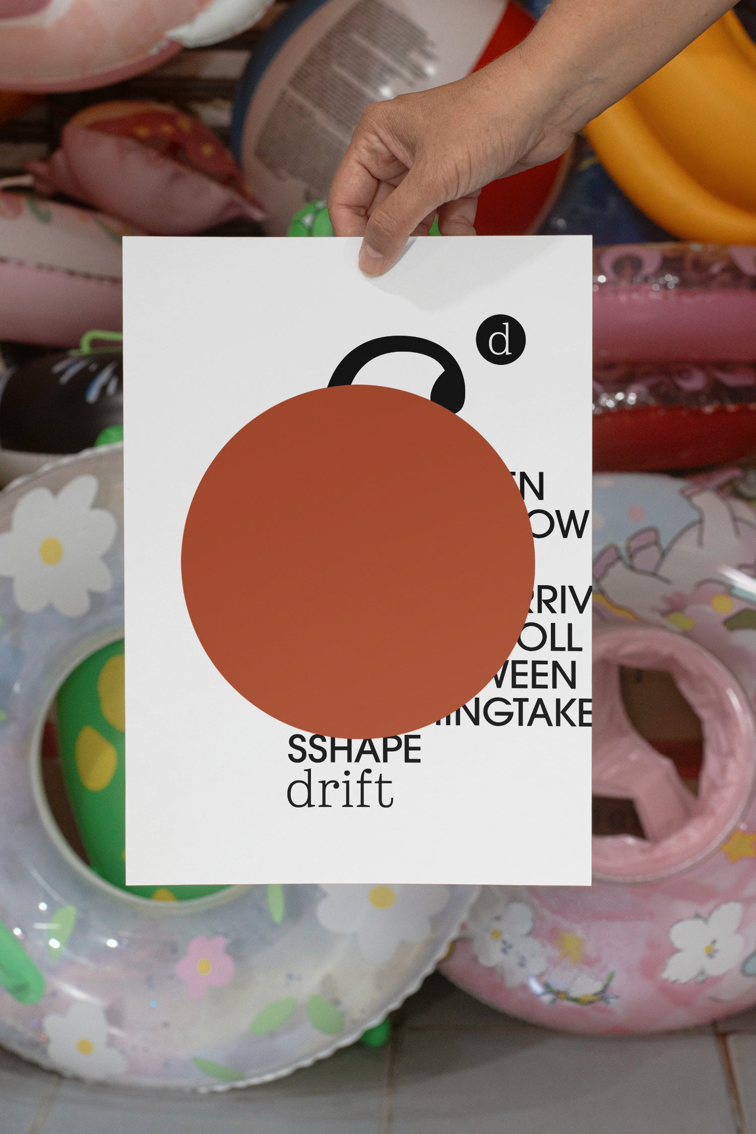 Poster mockup held by hand against a backdrop of several colorful plastic swim rings. Built for showcasing posters, editorial layouts, typography, branding, and print concepts.