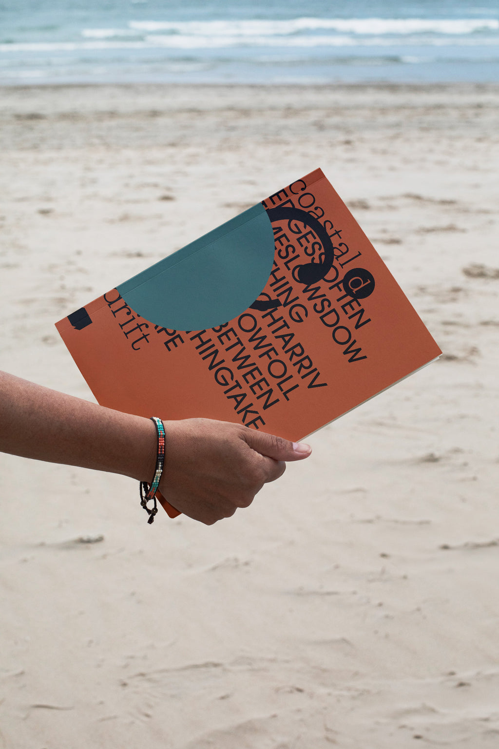 Softcover magazine mockup held against a sandy beach backdrop. Built for showcasing editorial layouts, magazines, branding, photography, and print concepts.