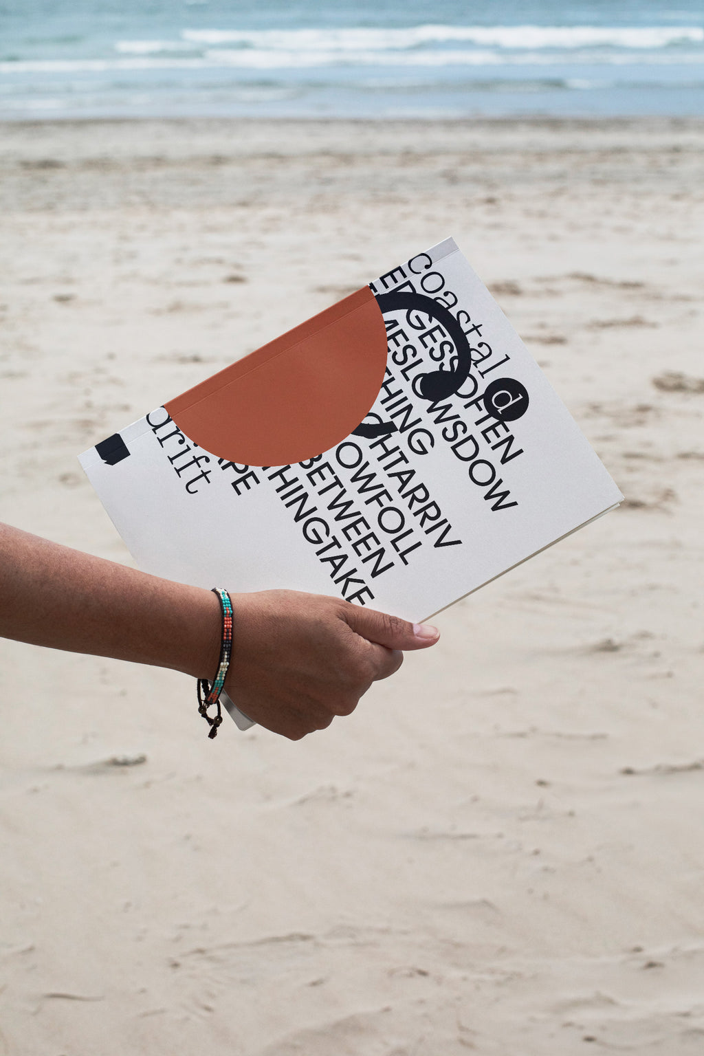 Softcover magazine mockup held against a sandy beach backdrop. Built for showcasing editorial layouts, magazines, branding, photography, and print concepts.