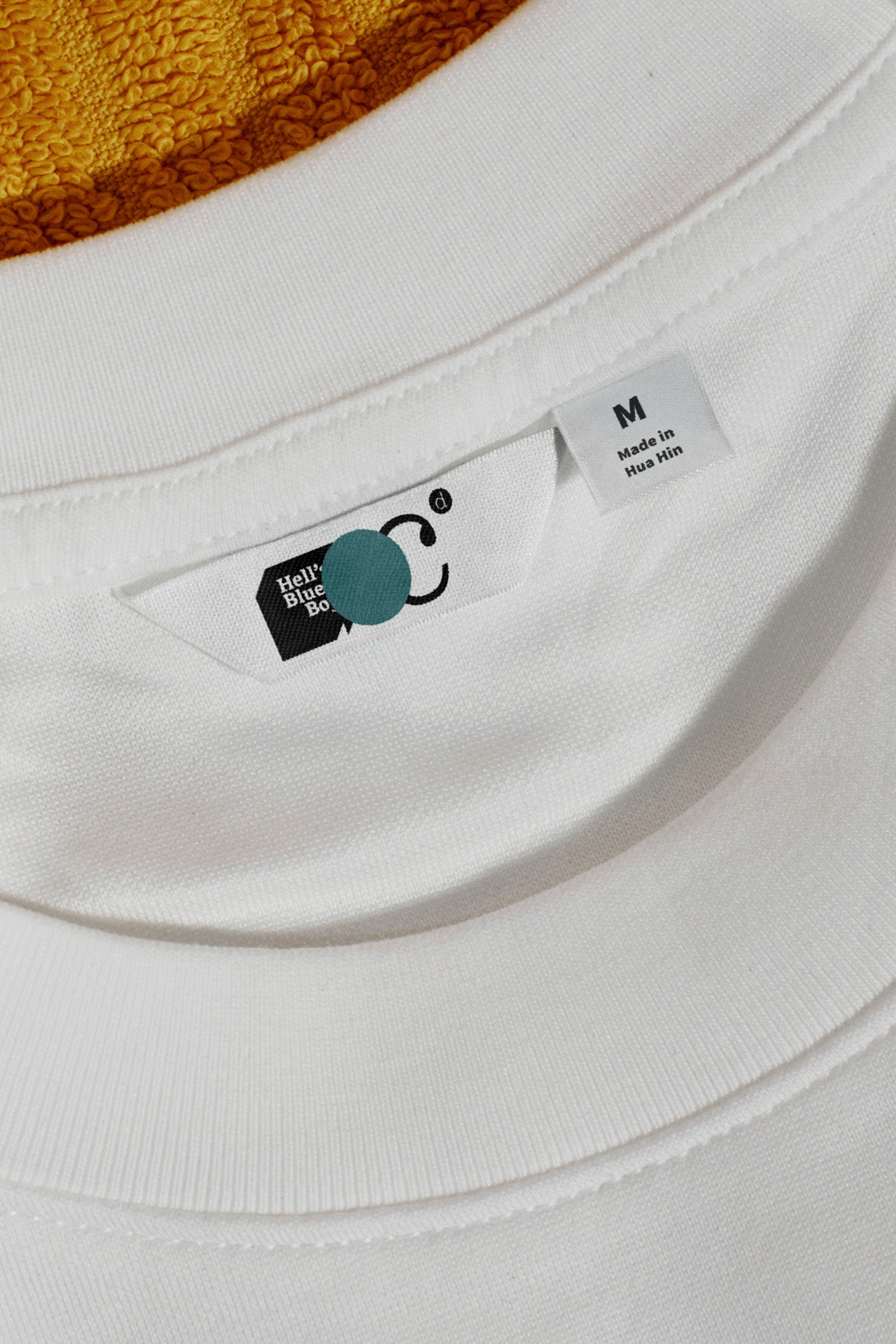 Close-up of a T-shirt label mockup resting on a beach towel. Built for showcasing woven labels, apparel branding, garment details, and fashion identities.