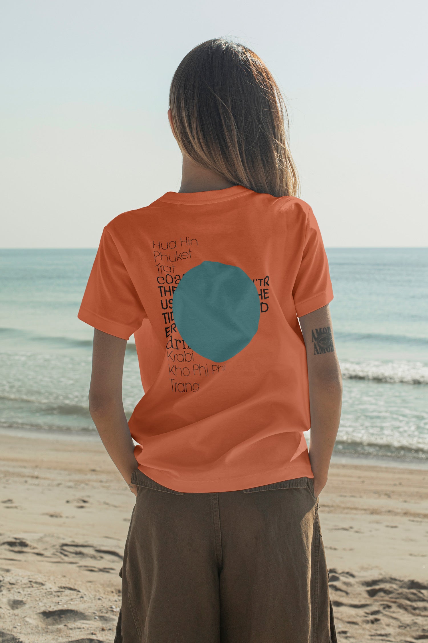 Fashion T-shirt mockup shown from the back while facing the open ocean. Built for showcasing back graphics, apparel branding, fashion collections, merchandise, and lifestyle identities.