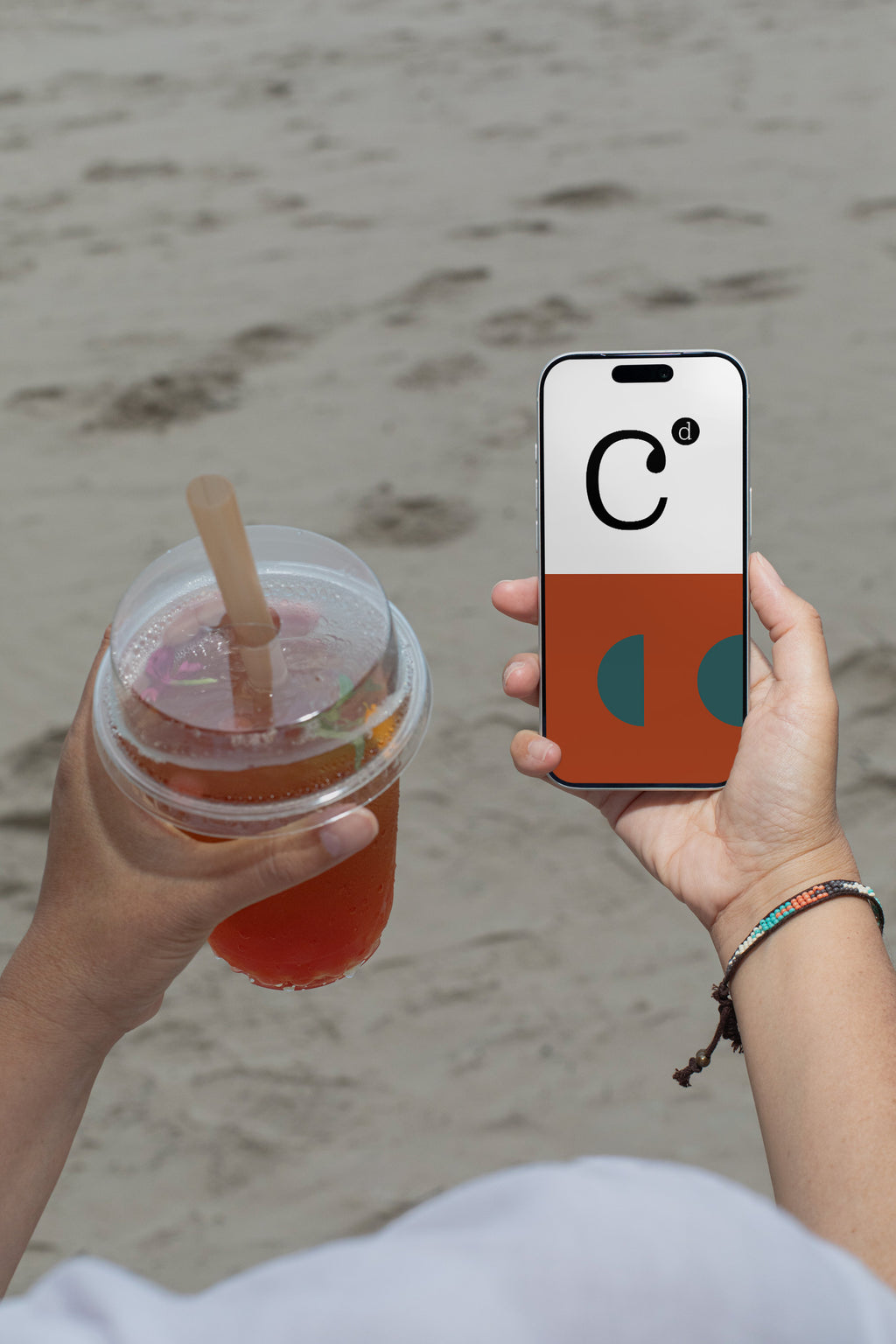 iPhone mockup held by hand with soda cup against a sandy beach backdrop. Built for showcasing app interfaces, branding, editorial layouts, illustrations, and creative presentations.