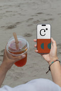 iPhone mockup held by hand with soda cup against a sandy beach backdrop. Built for showcasing app interfaces, branding, editorial layouts, illustrations, and creative presentations.