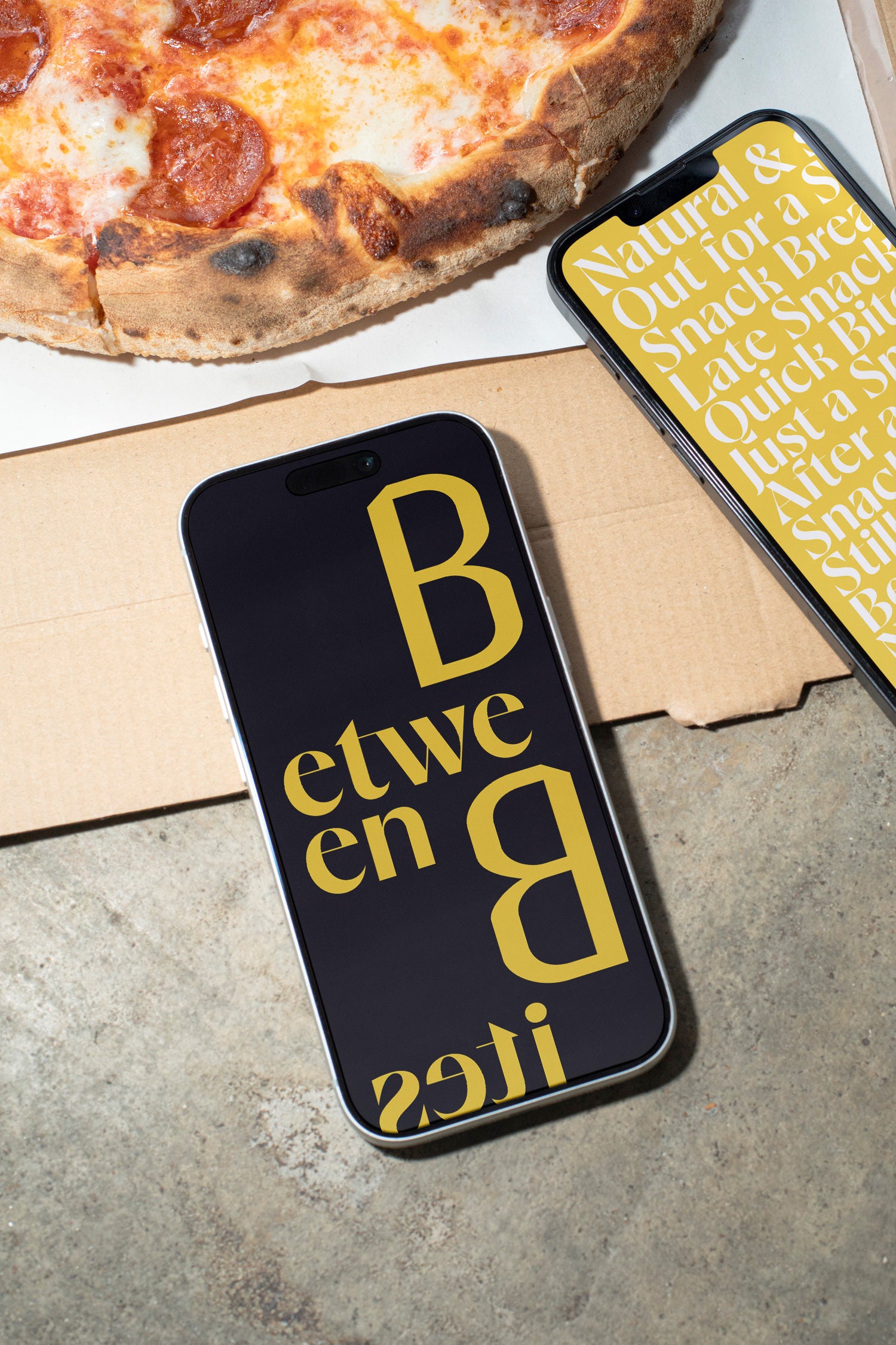 Two iPhones lying on a concrete table beside pizza and a takeaway box.
